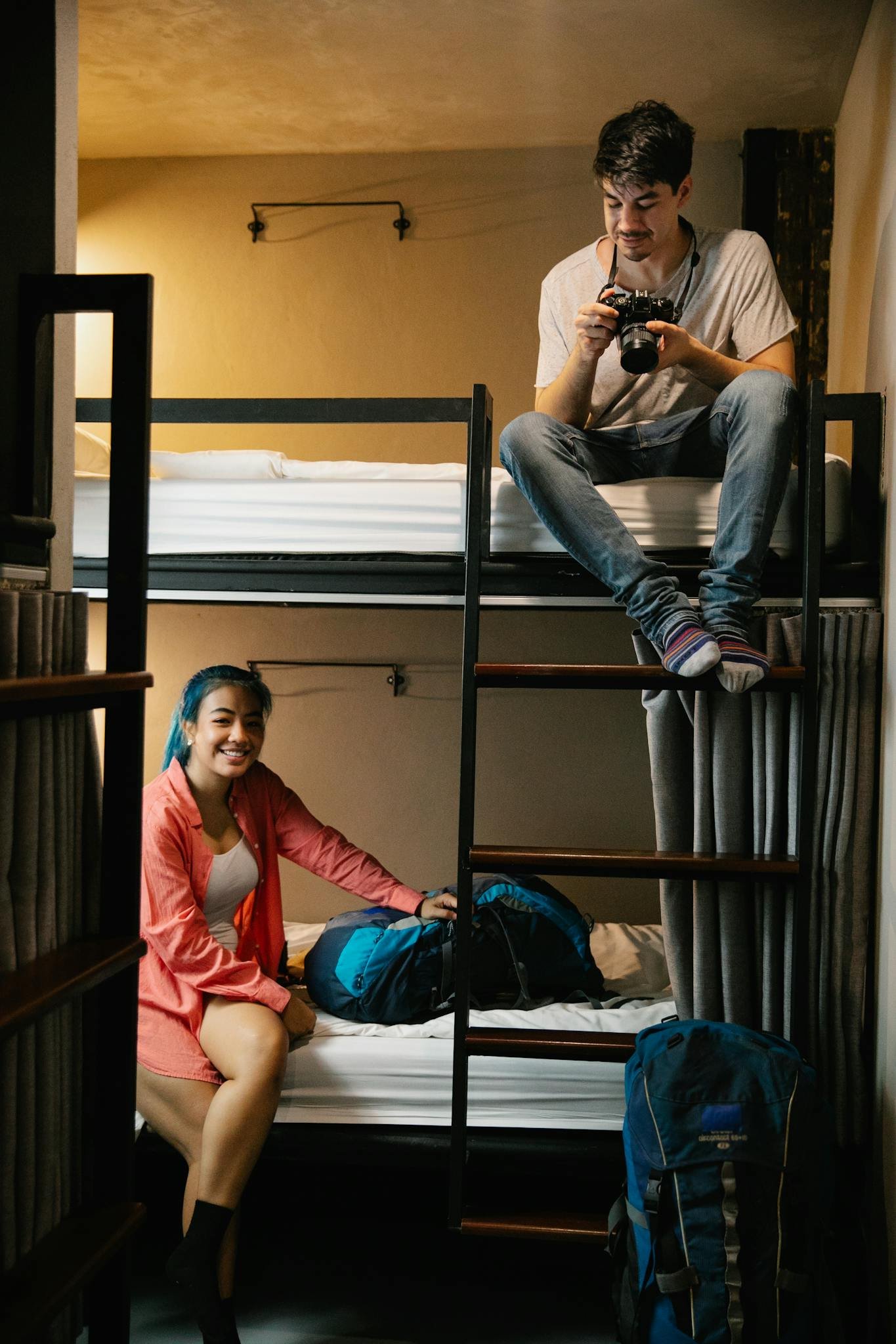 Two young travelers enjoying their hostel stay with bunk beds and backpacks.
